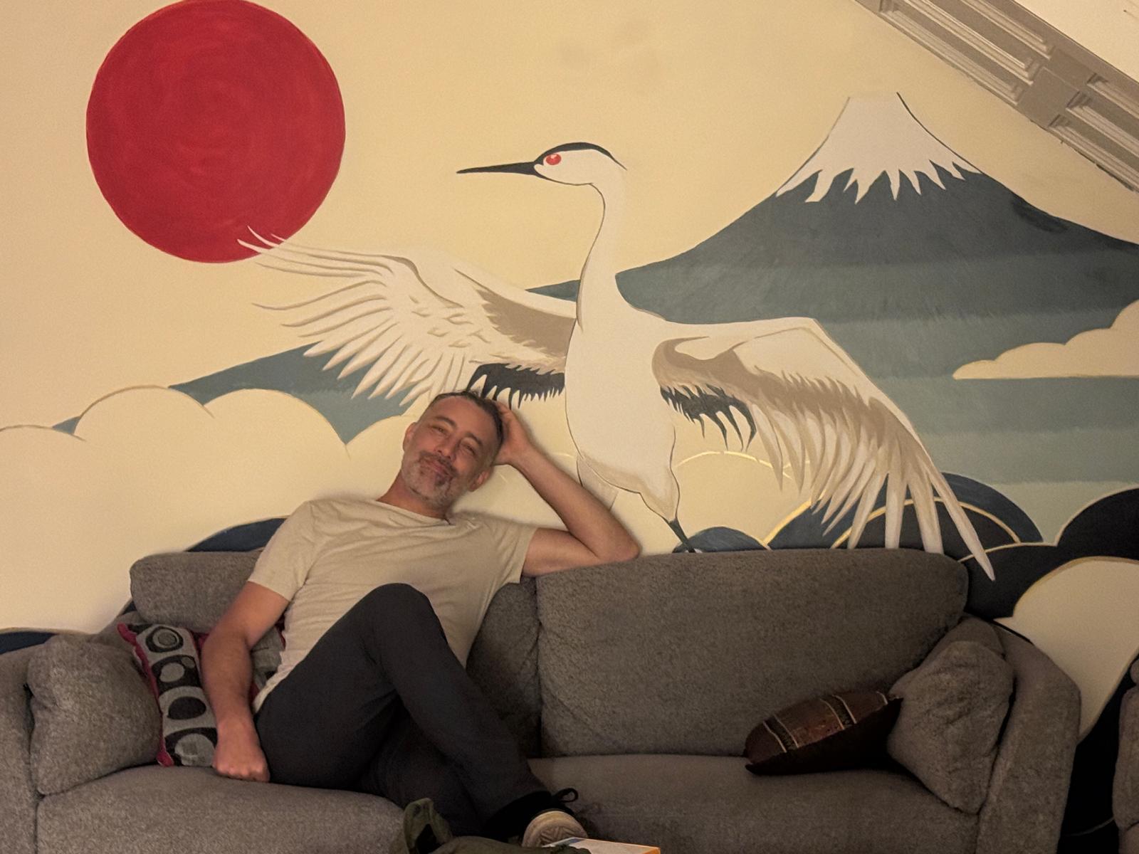 Host seated in front of a Japanese crane mural with a red sun and Mount Fuji